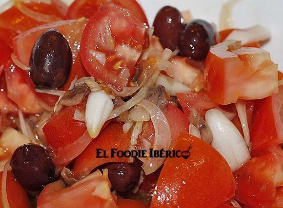 ensalada de tomates, anchoas, aceitunas kalamata y cebolla cortada en juliana